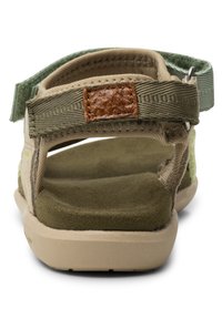 Beige sandaalit vihreillä akseteilla, kangasremmit ja ruskea nahkatäplä. Muotoiltu kumipohja, jossa on teksturoitu vihreä sisäpohja. Avoin takaosa.