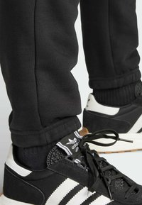 Svarta träningsbyxor kombinerade med svartvita sneakers med texturerad ovandel, tre vita ränder och svarta skosnören.