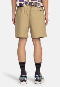 Pantalones cortos beige hechos de una tela ligera con una cintura elástica, que cuentan con un bolsillo trasero y un corte limpio y recto.