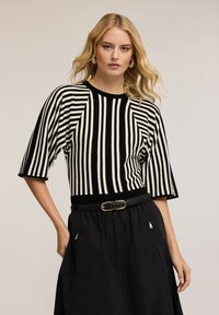 Zwart-wit gestreepte gebreide trui met korte mouwen, ronde hals en geribde randen. Draagt met een zwarte rok en bijpassende riem.