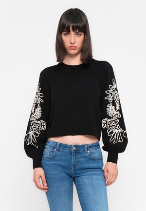 Zwarte cropped trui met lange, gebroken mouwen met witte bloemenborduursels op beide mouwen. Zachte textuur, geribbelde halslijn en manchetten.