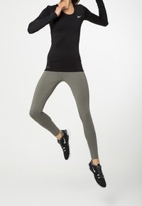 Musta pitkähihainen urheiluotsa Nike-logolla, yhdistettynä istuviin, teksturoituihin oliivinvihreisiin legginsseihin ja mustiin urheilukenkiin.