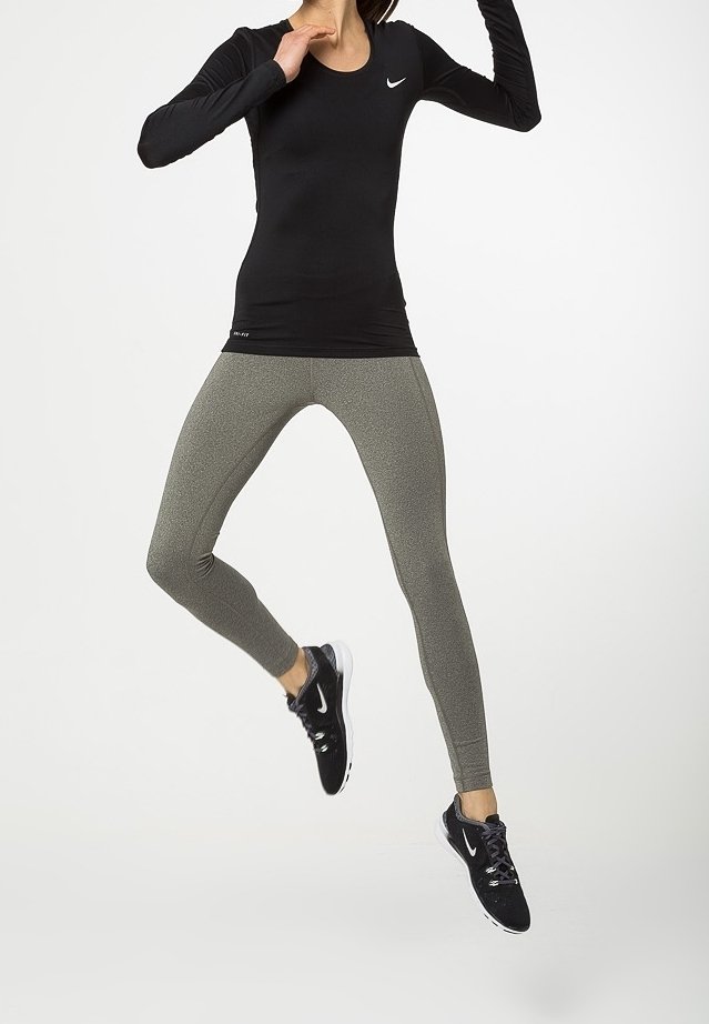 Musta pitkähihainen urheiluotsa Nike-logolla, yhdistettynä istuviin, teksturoituihin oliivinvihreisiin legginsseihin ja mustiin urheilukenkiin.