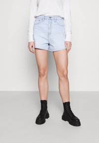 Ljusblå denimshorts med hög midja och upprullade kanter, i kombination med svarta snörkängor och en långärmad vit topp.