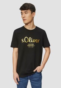 Zwarte katoenen T-shirt met een gouden opdruk van het logo en de tekst "s.Oliver ELEVATED ESSENTIALS SINCE 1969"; ronde hals, korte mouwen.