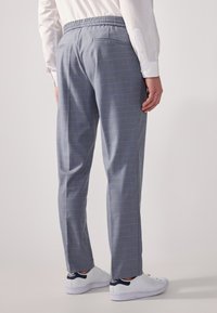 Grau karierten Hosen mit einem elastischen Bund, die ein dezentes blaues Karomuster und zwei Gesäßtaschen aufweisen, kombiniert mit weißen Sneakers.