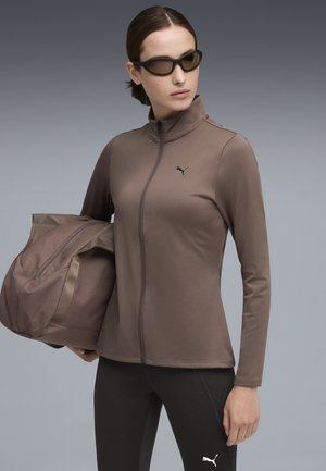 Brown zip-up jacket made of smooth fabric, featuring a subtle logo, paired with black leggings and a matching gym bag.