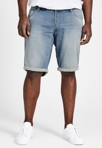 Shorts de mezclilla en azul claro, con un acabado desgastado, puños enrollados y un diseño clásico de cinco bolsillos, combinados con zapatillas blancas.