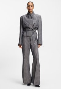 Costume sur mesure à rayures grises, comprenant une veste cintrée croisée avec une ceinture à nouer et un pantalon à jambes larges. Tissu lisse avec des accents élégants et minimalistes.