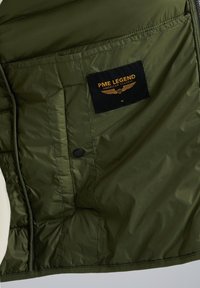Olivegrön isolerad jacka med svart etikett som läser "PME LEGEND AMERICAN CLASSIC M." Har knäppning och quiltad textur.
