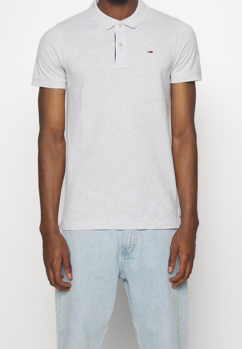 Polo en coton gris avec col, patte de boutonnage à deux boutons, et petit logo brodé. Associé à un jean en denim bleu clair.