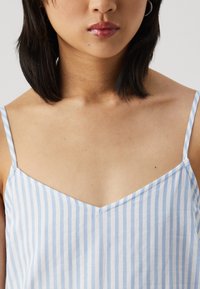 Μπλε και λευκό ριγέ καμισόλ με λεπτές τιράντες, διαθέτοντας V λαιμόκοψη και απαλή, ελαφριά υφή υφάσματος.