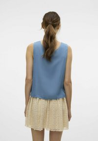 Blå ärmlös topp i lätt tyg, ihop med en kr ämfärgad spetskjol med ett cirkulärt mönster och vågig nederkant.