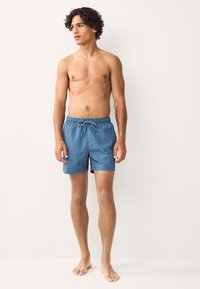 Siniset kuviolliset uima-shortsit, joissa on joustava vyötärönauha ja kiristysnaru. Valmistettu kevyestä kankaasta, polvipituiset ja väljät.