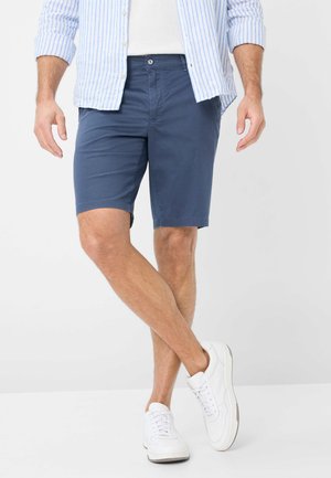 Kneehohe dunkelblaue Shorts aus einem Baumwoll-Mischgewebe, mit geradem Schnitt und seitlichen Taschen, kombiniert mit weißen Sneakers und einem hellblau gestreiften Hemd.