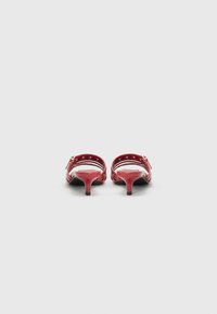 Sandalias de tacón de charol rojo con tiras ranuradas y detalles de hebilla, con un tacón delgado y una textura suave.