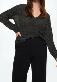 Top nero a maniche lunghe con scollatura a V, realizzato in un tessuto scintillante e testurizzato. Abbinato a pantaloni neri a vita alta.