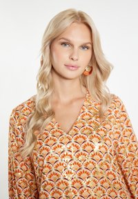 Bluză colorată cu un model floral în nuanțe de portocaliu, roșu și auriu pe un fundal deschis. Decupaj în V, material moale și siluetă fluidă.