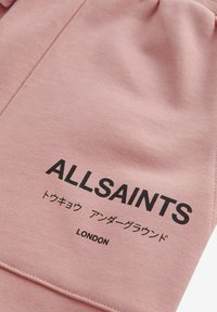 Růžová bavlněná látka s hladkým strukturováním, se černě potištěným nápisem „ALLSAINTS“ a japonskými znaky. Design zahrnuje pasový lem.