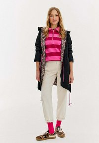 Černá bunda s podšívkou leopardího vzoru, růžový a červený pruhovaný polo, krémové kalhoty a boty s leopardím vzorem a růžovými ponožkami.