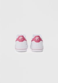 Valkoiset Nike Air -tennarit, joissa on vaaleanpunaiset yksityiskohdat takana. Niissä on sileä pinta, pyöreä muoto ja näkyvä logo kantapäässä.