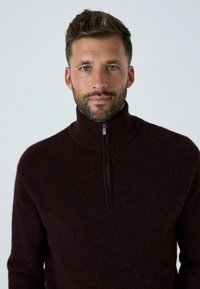Burgunderfarbener Halb-Zip-Pullover aus strukturiertem Strickstoff. Verfügt über einen hohen Kragen und einen Reißverschluss am Hals, der einen gemütlichen Sitz bietet.