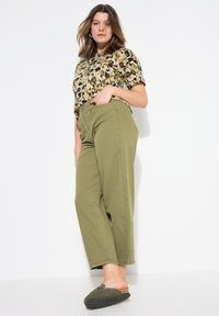 Camisa de manga corta de estampado de leopardo en beige y negro combinada con pantalones de cintura alta en verde oliva, completada con zapatillas verdes tipo slip-on.