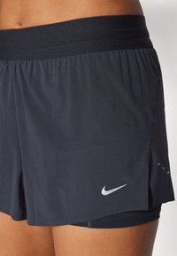 Musta urheiluhousut, joissa on leveä joustava vyötärö. Väriin kuuluu Nike-logo ja halkio suunnittelussa helman osalta liikkumisen helpottamiseksi.