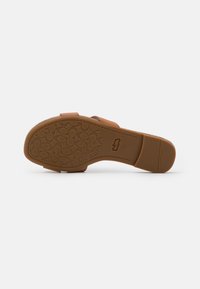 Brun slip-on sandal med gummisål, der har en tekstureret, mønstret bund og minimalistisk design. Justerbar stropdetalje.