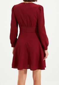 Röd texturerad klänning med figursydd midja och långa puffärmar, med en dragkedja i ryggen och en utsvängd kjol som slutar ovanför knäet.