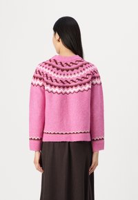 Rosa stickad tröja med ett fair isle-mönster i brunt och vitt vid halsringningen och fållen, med en avslappnad passform och långa ärmar.