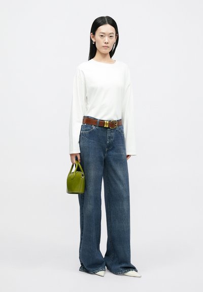 Biała koszula z długim rękawem, brązowy pasek ze złotym okuciem, szerokie dżinsy o niebieskim kolorze i mała zielona torebka. Białe buty na szpic.