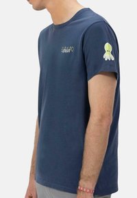 Camiseta de algodón azul marino de manga corta, con un pequeño logo impreso y un pulpo verde bordado en la manga izquierda.