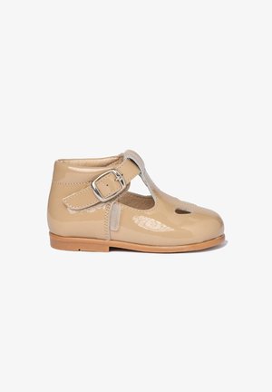 Zapato T-bar de cuero sintético beige con cierre de hebilla, punta redonda, diseño recortado y suela de cuero marrón claro. Textura suave.