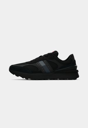 Black athletic shoes with mesh and suede materials, featuring a thick sole, logo accent, and gray stripe detail on the side.