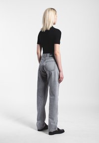 Helle graue High-Waist-Jeans mit geradem Bein, versehen mit hinteren Taschen und dezenten Ausbleichungen, kombiniert mit einem schwarzen Kurzarmoberteil.