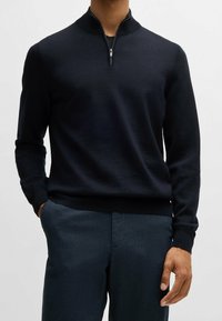 Marinblå halvzip-tröja med långa ärmar, ribbade muddar och en texturerad yta. Kombinerad med mörkgrå byxor.