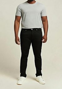 Šedé tričko s krátkým rukávem, černé elastické džíny a bílé tenisky. Outfit se vyznačuje jednoduchými liniemi a klasickou barevnou paletou.