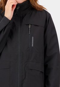 Jachetă waterproof neagră cu un buzunar cu fermoar pe piept și două buzunare frontale. Dispune de un guler înalt și o branduire subtilă pe față.