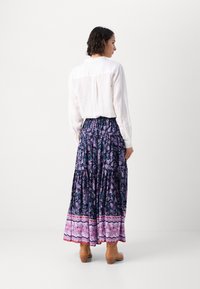 Jupe longue à volants avec un motif floral bleu marine et des accents roses. Associée à une chemise en lin blanche et des bottines marron.
