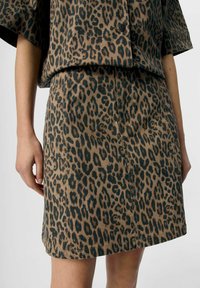 Brun leopardmönstrad kjol med svarta fläckar, har en rak skärning och sid sömsdetaljer, tillverkad av ett texturerat tyg.