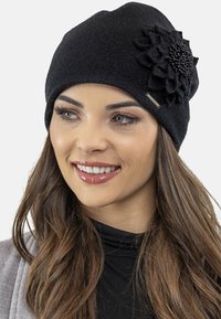 Bonnet tricoté noir avec une accent en fleur en tissu ornée de perles. Texture douce, design ajusté et une petite étiquette de marque en métal sur le côté.