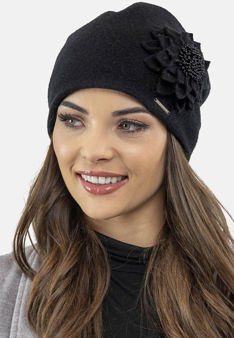 Bonnet tricoté noir avec une accent en fleur en tissu ornée de perles. Texture douce, design ajusté et une petite étiquette de marque en métal sur le côté.