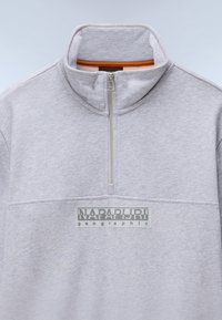 Ανοιχτό γκρι φούτερ με λαιμόκοψη μισή φερμουάρ, πορτοκαλί λεπτομέρεια στο εσωτερικό του γιακά και εμφανές γκρι λογότυπο στο μπροστινό μέρος. Μαλακή υφή.