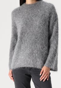 Grauer, flauschiger Pullover mit rundem Ausschnitt und langen Ärmeln. Aus weichem Material hergestellt, mit lockerer Passform, verfügt über einen Saum, der leicht geschwungen ist.