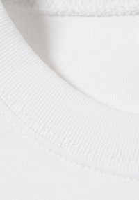 White cotton shirt collar, featuring a ribbed texture and smooth finish. Seam detail visible on the edge, highlighting the garment's construction.