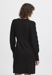 Svart stickad klänning med texturerade kabelstickade ärmar. Tätt sittande bodice och utsvängd kjol. Slät tyg med ribbade ärmslut och halsringning.