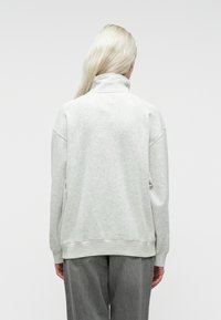 Pull léger gris clair avec un col haut, coupe ample et poignets côtelés. Texture douce, design minimal et sans motifs ni accessoires visibles.