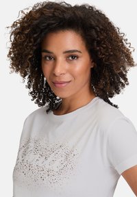 Hvid kortærmet t-shirt med et pletteret mønster i beige og brune nuancer på fronten. Glat stof og afslappet pasform design.