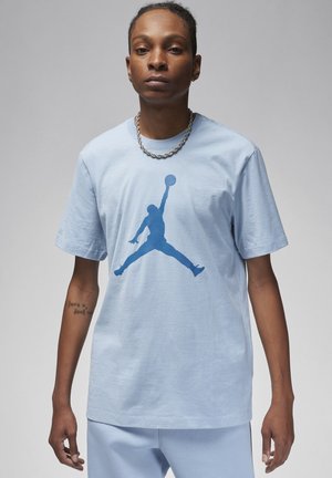T-shirt in cotone blu chiaro con una grande silhouette blu del logo Jordan al centro. Maniche corte e scollatura rotonda. Design semplice.